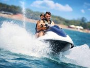 Young couple driving a blue and white jet ski in the ocean next to a beach
