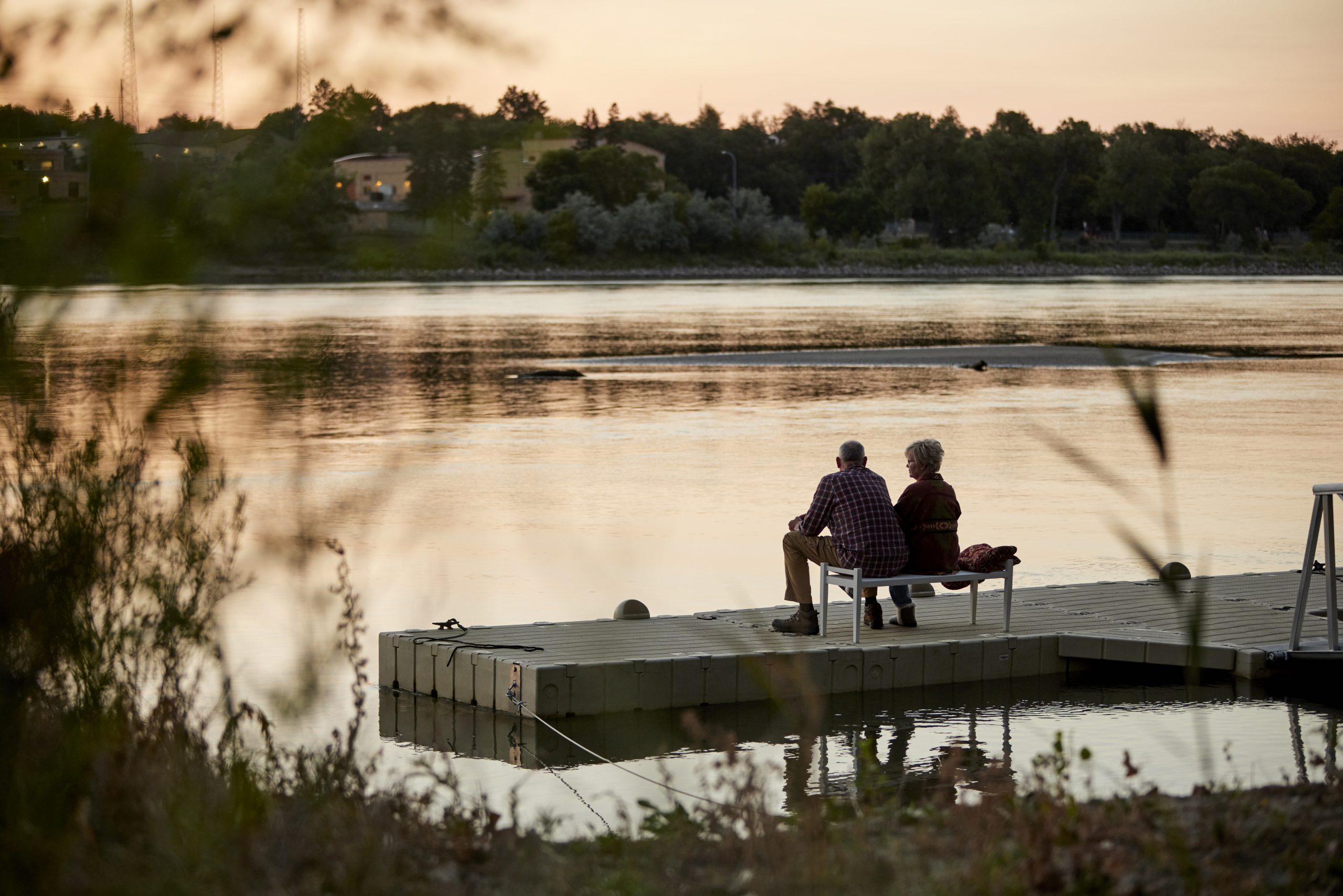 wide angle shot of older couple sitting on floating dock at sunset