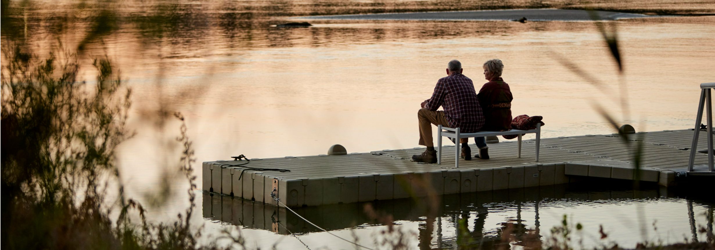 older couple sitting on floating dock at sunset