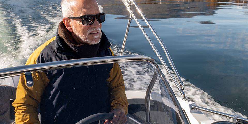 Older man in a heavy coat driving a boat over a calm lake during winter